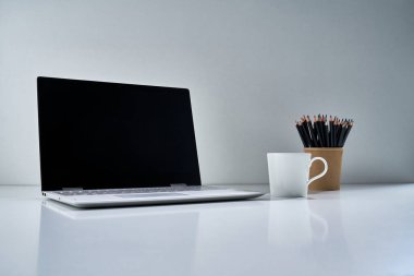 Modern bir dizüstü bilgisayar, beyaz bir fincan ve açık gri arka planda narin bir buket çiçekli diğer eski şeyler.