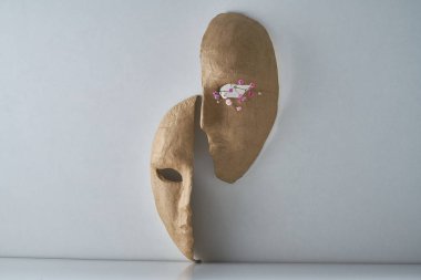 Açık gri arka planda kağıt maskelerin yarısına sahip kompozisyon ve narin bir buket çiçek.