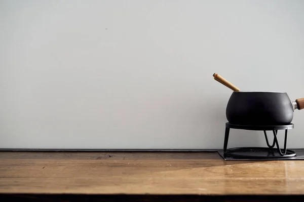 Kitchen scene black pan for cooking fondue stands on a wooden table on a black background