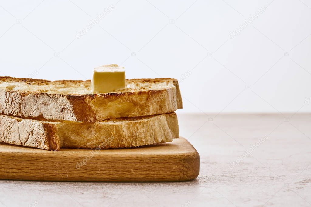 Slices of fried freshly baked bread with a piece of butter on top, lie on a wooden shelf on a marble table