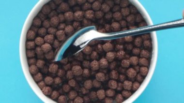 Gümüş bir kaşık, mavi arka planda beyaz bir fincanda çikolatalı süt toplarını karıştırır.