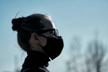 Siyah koruyucu maskeli ve siyah güneş gözlüklü genç kız, virüse karşı korunuyor.