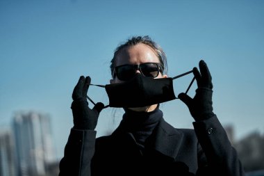 Siyah koruyucu maskeli ve siyah güneş gözlüklü genç kız, virüse karşı korunuyor.