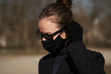 Siyah koruyucu maskeli ve siyah güneş gözlüklü genç kız, virüse karşı korunuyor.