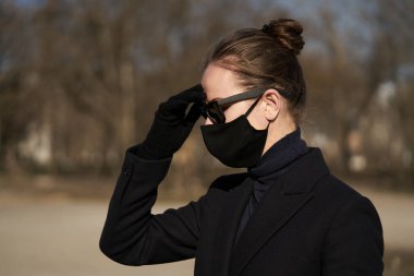 Siyah koruyucu maskeli ve siyah güneş gözlüklü genç kız, virüse karşı korunuyor.
