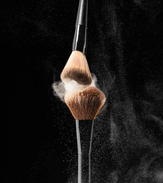 Natural bristle makeup brushes with splash of makeup powder on black background