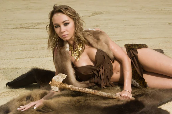 Prehistoric woman with the stone axe is sitting on the fur — Stock Photo, Image