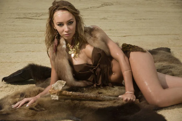 Prehistoric woman with the stone axe is sitting on the fur — Stock Photo, Image