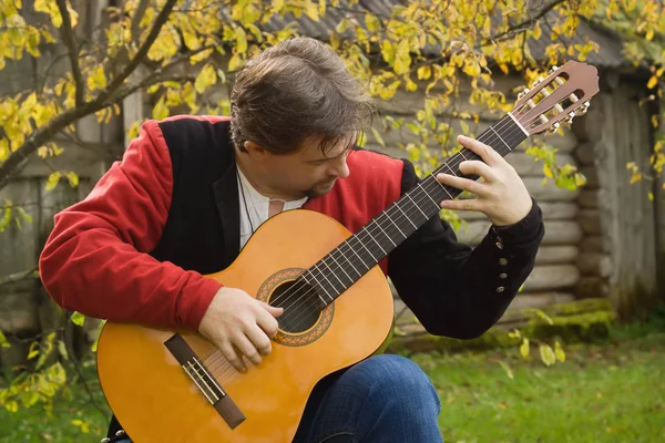 Člověk hraje na kytaru v podzimní zahradě — Stock fotografie