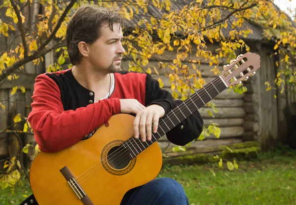 Hombre tocando la guitarra en el jardín de otoño —  Fotos de Stock
