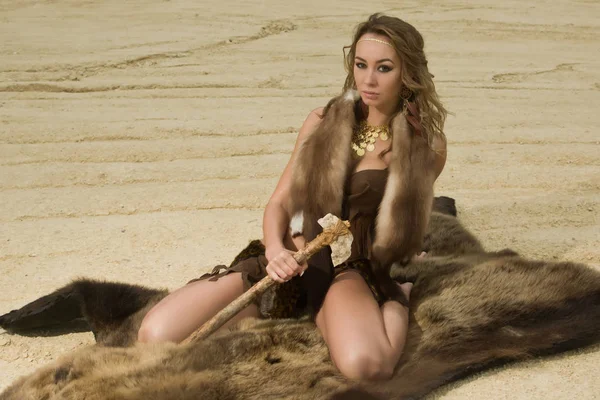 Prehistoric woman with the stone axe is sitting on the fur Stock Photo