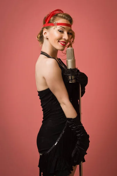 Bela atriz em vestido retro preto cantando com microfone — Fotografia de Stock