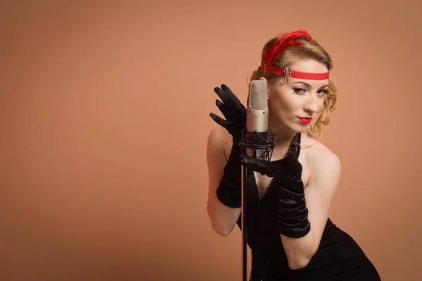 Bela atriz em vestido retro preto cantando com microfone — Fotografia de Stock