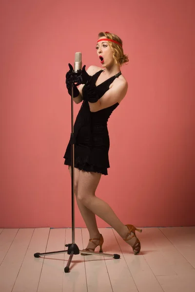 Pretty actress in black retro dress singing with microphone — Stock Photo, Image