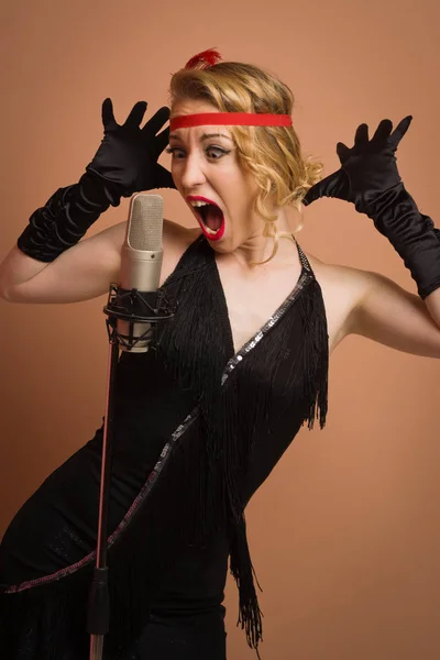 Linda actriz en vestido retro negro cantando con micrófono —  Fotos de Stock