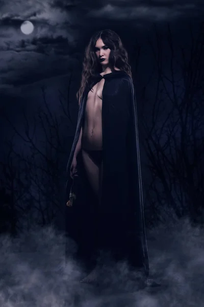 Bella ragazza gotica in un mantello nero contro un paesaggio notturno — Foto Stock