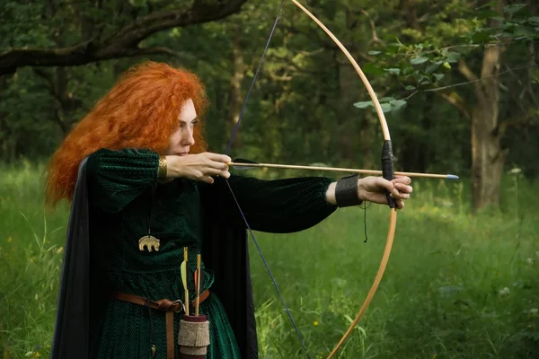 Red haired girl shoots from the bow — Stock Photo, Image