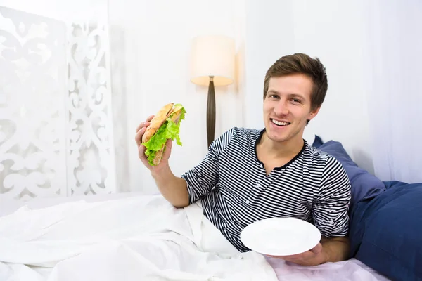 Pria lajang makan di tempat tidur — Stok Foto