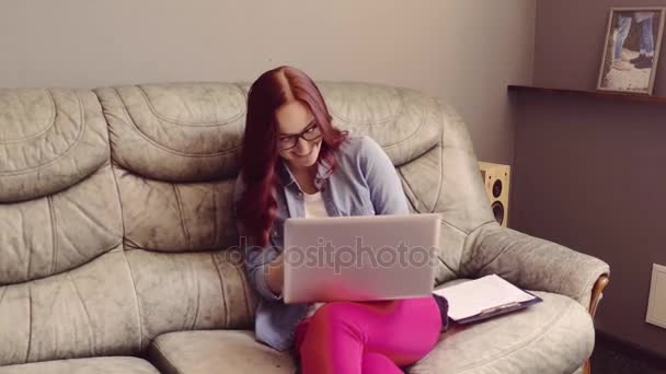 Freelancer red haired female sitting oh sofa, working and answering phone. — Stock Video