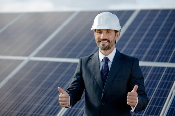 Empresário mostrando polegares para cima, painéis solares atrás dele . — Fotografia de Stock
