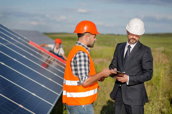 Businessman signing contract with foreman, technician examining solar panels at backdrop. — Stock Photo, Image