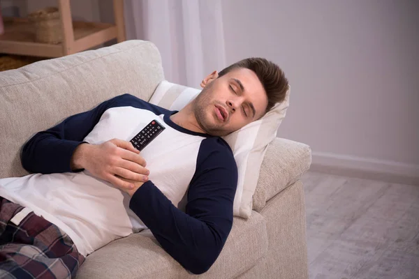 Człowiek śpi na kanapie z Tv remote w jego rękach. — Zdjęcie stockowe
