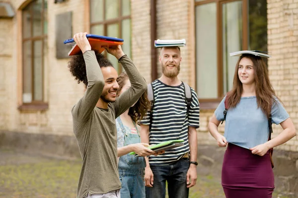 Estudantes se divertindo, segurando livros sobre cabeças . — Fotografia de Stock