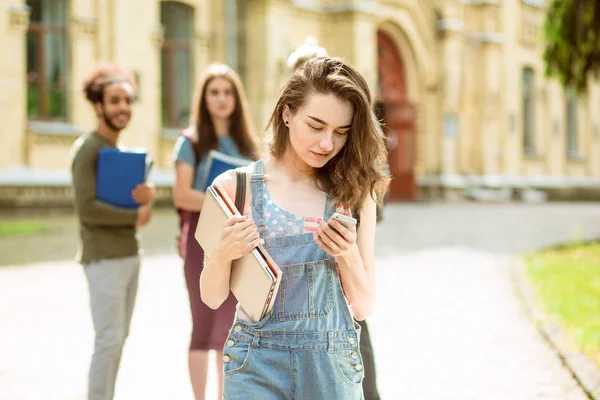 På förgrunden student tjej i denim med telefon och anteckningsböcker i hennes händer. — Stockfoto