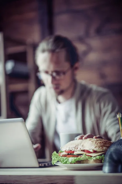 Freelancer digitando com uma mão, segurando outra mão para sandwi — Fotografia de Stock