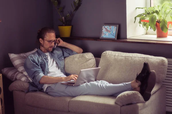 Freelancer na kanapie, rozmów telefonicznych, trzymając laptop na kolanach. — Zdjęcie stockowe