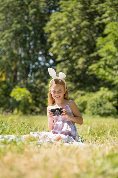 Kleines hübsches Mädchen sitzt auf Decke und hält Kamera. — Stockfoto