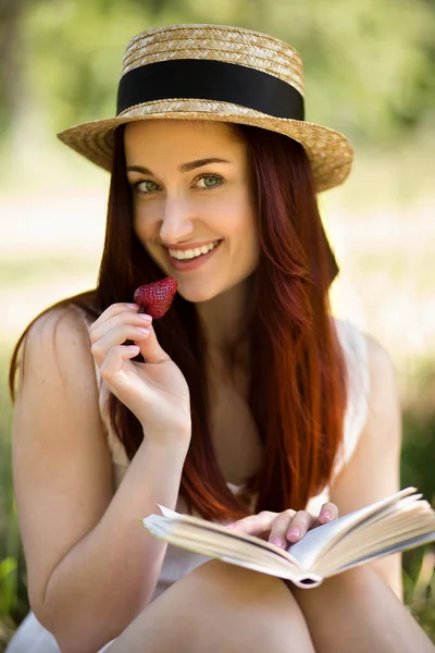 Romantikus fiatal hölgy a kertben, eper eszik, és könyvet olvas. — Stock Fotó