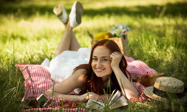 Vista frontale di zenzero ragazza sorridente sdraiato su coperta su erba verde . — Foto Stock