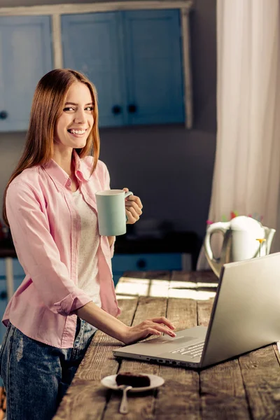 Ragazza felice che lavora sul computer portatile mentre beve caffè o tè . — Foto Stock