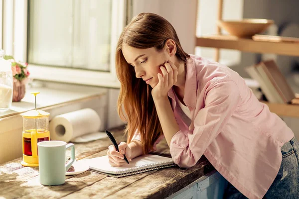 Retrato de niña escribiendo en cuaderno, de pie en la cocina . — Foto de Stock