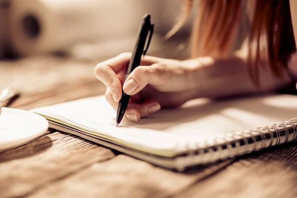 Close-up van dames hand schrijven met pen op notebook op houten tafel. — Stockfoto