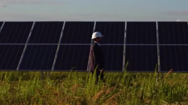 Vista lateral del director de la estación de energía solar caminando y comprobando los paneles fotovoltaicos . — Vídeo de stock