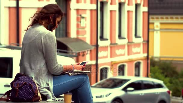 Video con una joven turista sentada en un parapeto en el centro de la ciudad . — Vídeos de Stock