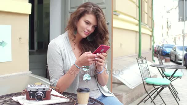 Junge reisende Frau mit lockigem Haar tippt SMS auf Smartphone. — Stockvideo