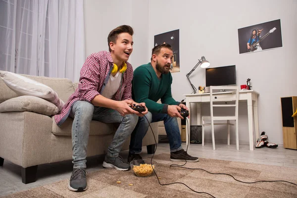 Vista lateral do pai e do filho adolescente sentado no sofá, jogando videogames . — Fotografia de Stock