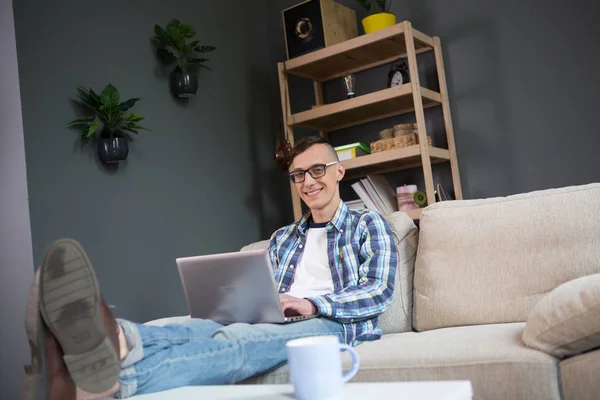 Πορτρέτο του νέος ελεύθερος επαγγελματίας άνδρας κάθεται στο καναπέ, πληκτρολόγησης σε φορητό υπολογιστή. — Φωτογραφία Αρχείου