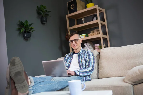 Retrato del joven freelancer sentado en el sofá teclados en el portátil . — Foto de Stock