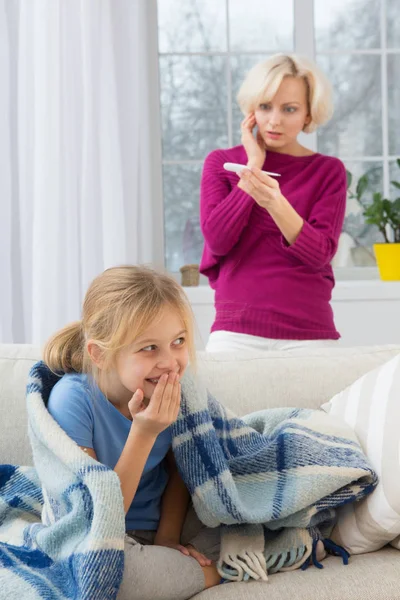 Ziek meisje onder de deken glimlachen, betrokken moeder op achtergrond. — Stockfoto