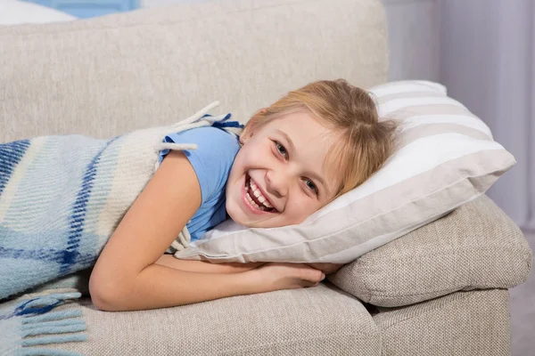 Małej dziewczynki, chory leżąc na kanapie i uśmiechając się. — Zdjęcie stockowe