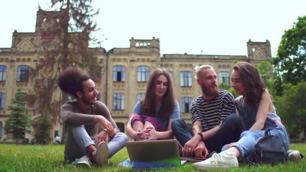 Glada unga college fiends sitter på gräsmattan framför universitet. — Stockvideo