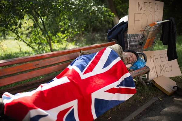 Homem sem-teto dormindo no banco, cobrindo com bandeira da Grã-Bretanha . — Fotografia de Stock