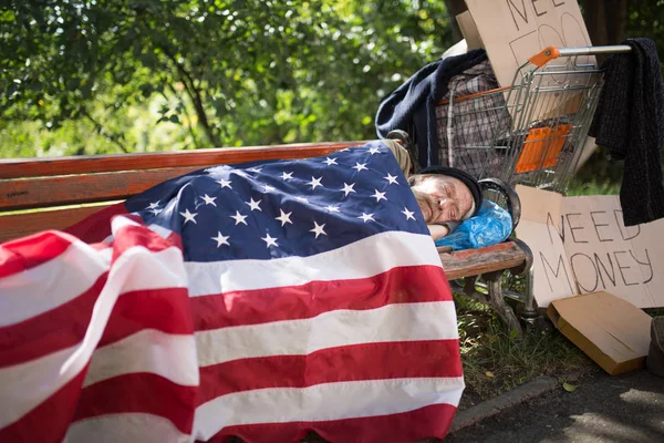 Homeless man using USA flag as a blanket.