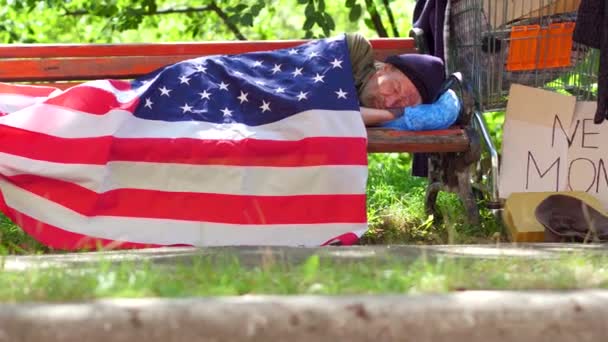 Перегляд бездомний чоловік лежить на лавці, покриті Прапор США. — стокове відео