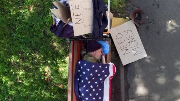 Draufsicht auf einen Bettler, der auf einer Bank liegt, bedeckt mit einer US-Fahne. — Stockvideo