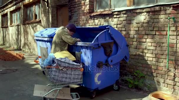 Footage with homeless man searching food and empty bottles in garbage. — Stock Video